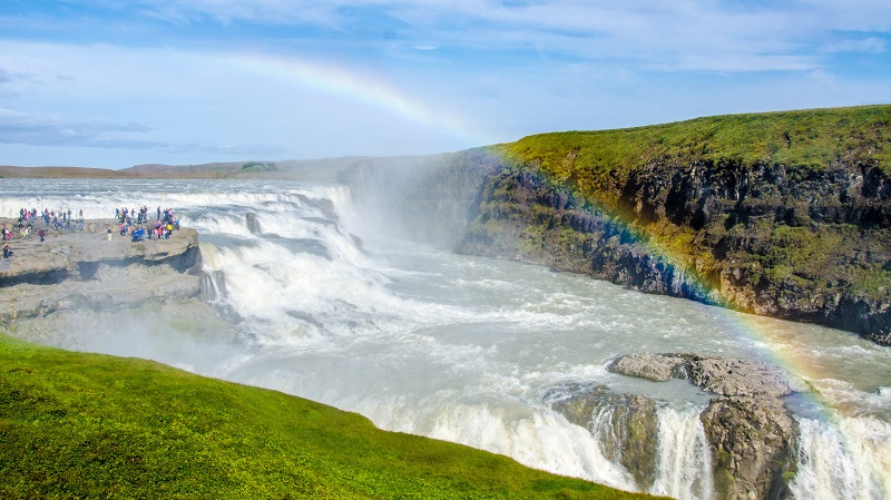 Den m�ktiga Gullfoss, med en regnb�ge genom hela bilden och gr�sgr�na omgivningar.