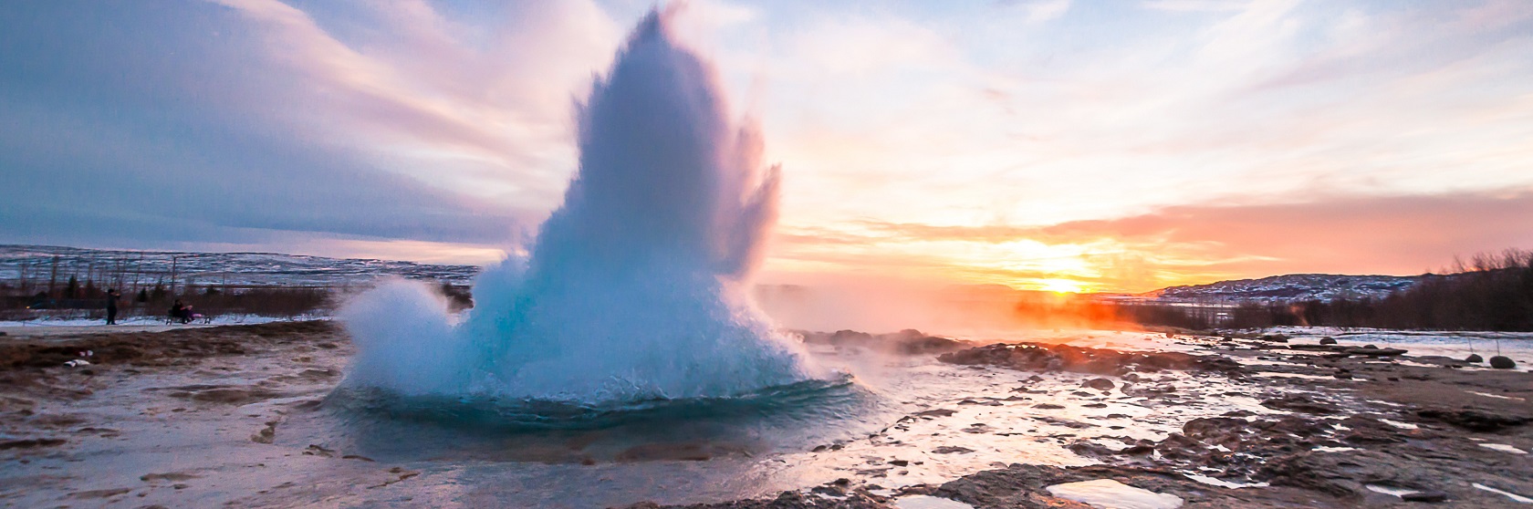 Geysern Strokkur skjuter upp en kaskad av kokhett vatten, mot en solnedg�ng med bl� himmel och utdragna rosaf�rgade moln.