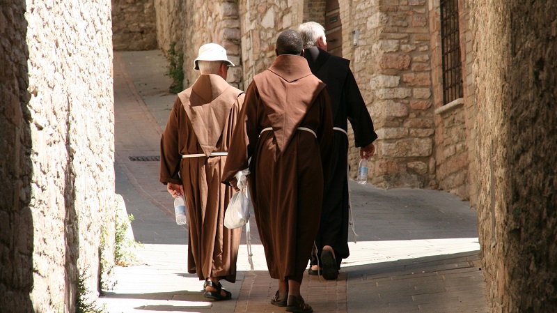 Tre brunkl�dda munkar vandrar bort�t, uppf�r en gr�nd i Assisi.