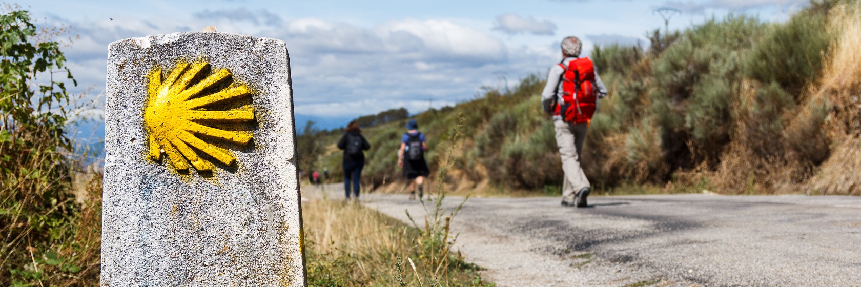 Den gula pilgrimssn�ckan visar v�gen f�r tre pilgrimsvandrare som g�r bort�t utmed en landsv�g.