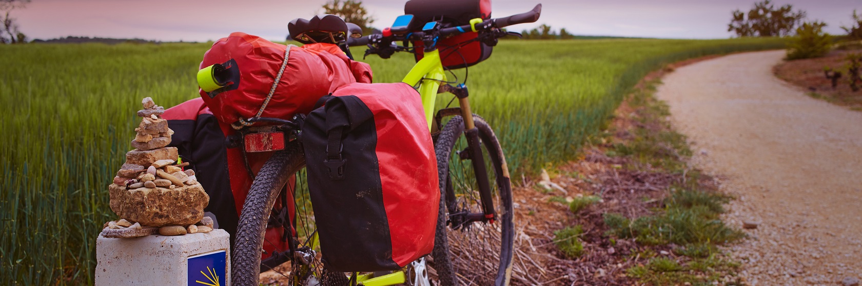 Mountain bike med r�da cykelv�skor parkerad vid en Caminov�gsten, med ett gr�nt f�lt i bakgrunden.