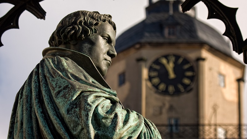 Kopparstaty av Martin Luther fr�n sidan i halvprofil, med ett suddigt kyrktorn i bakgrunden.