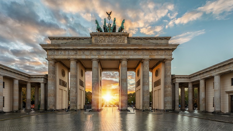 Solens sista str�lar lyser genom Brandenburger Tor-monumentet i Berlin, mot en himmel med utdragna moln.