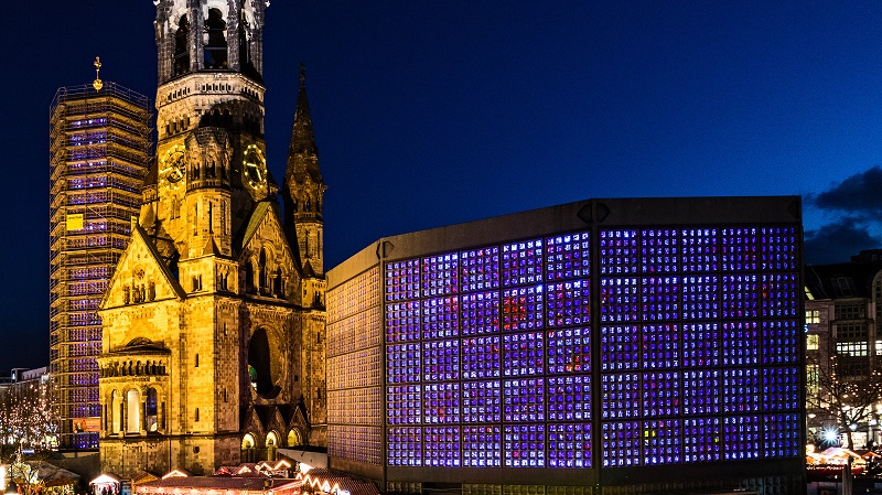 Resterna av Kaiser-Wilhelm-Ged�chtniskirche i Berlin, som skadades sv�rt under de allierades bombningar av Berlin 1943. Intill finns en modern hexagonal kyrka vars m�nga sm�f�nster lyses upp i olika f�rger.