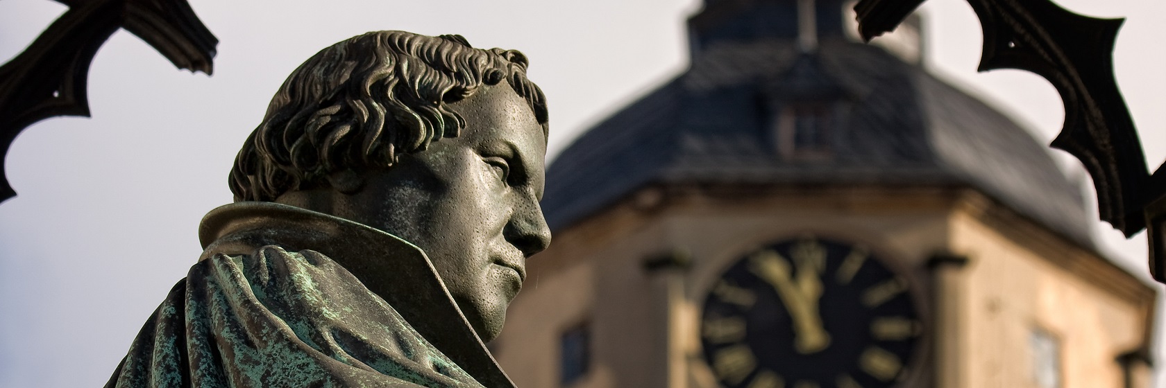 Kopparstaty av Martin Luther fr�n sidan i halvprofil, med ett suddigt kyrktorn i bakgrunden.